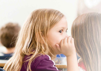 A little girl whispers into her friends ear
